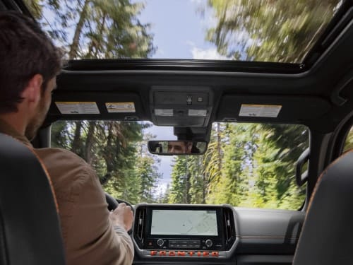 2026 Nissan Frontier interior view showing center screen and a forest view through the windshield and moonroof
