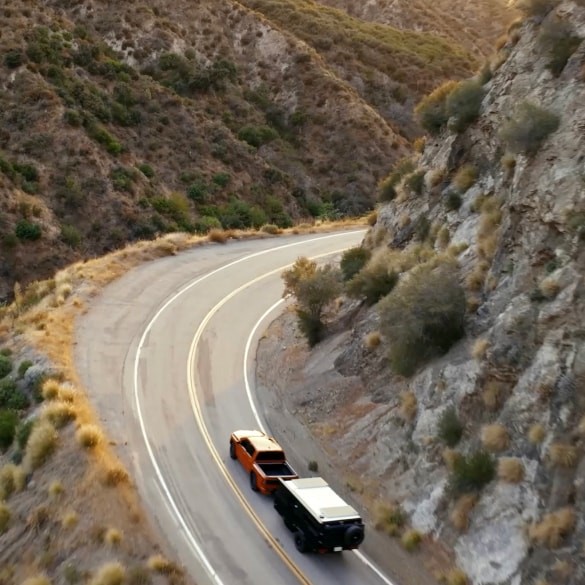 2026 Nissan Frontier in red towing a trailer up a mountain road curve