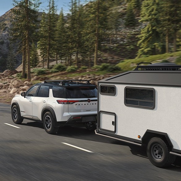 2026 Nissan Pathfinder towing a small enclosed trailer while driving on a highway.