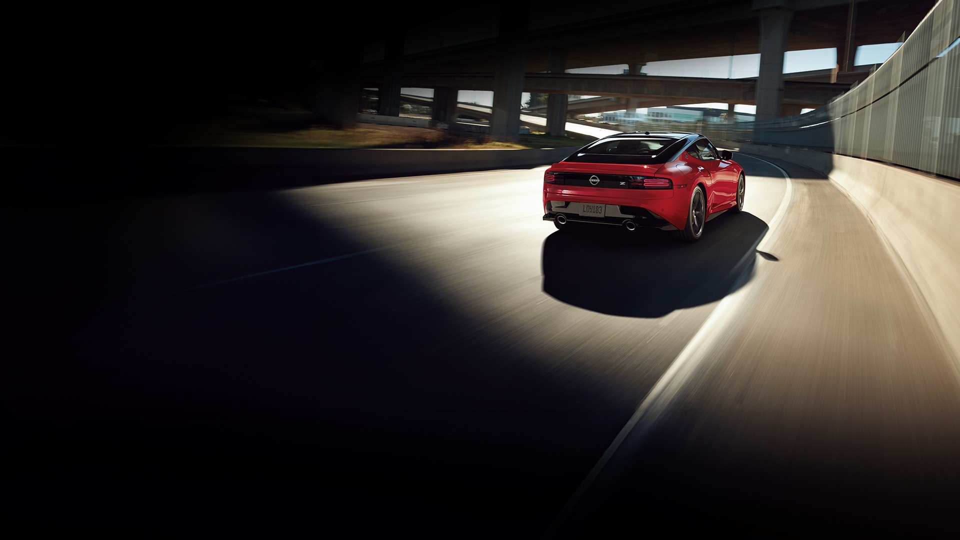 2026 Nissan Z rear view driving down a curved highway beneath a complex set of overpasses