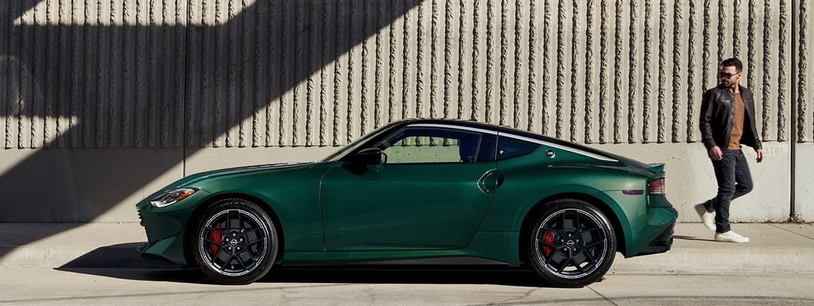 2027 Nissan Z in green, side view, parked in front of a concrete building with a pedestrian doing a double-take.